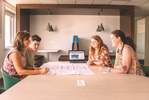 4 collega's aan een vergadertafel kijken naar een plan